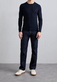 Marinblå långärmad tröja med rund halsringning, kombinerad med mörk denimjeans och krämfärgade sneakers, med en strukturerad finish och normal passform.