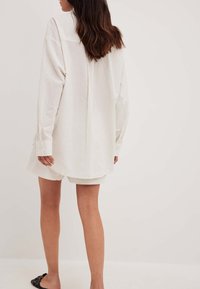White striped oversized shirt dress with long sleeves, featuring a rounded hem and a relaxed fit, paired with matching shorts.