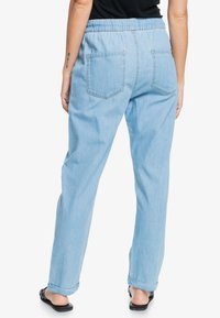 Pantaloni in denim blu chiaro con vestibilità rilassata, cintura elastica e due tasche posteriori. Il materiale è morbido e appare leggermente sbiadito.