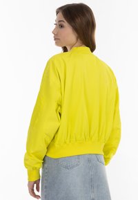 Giacca bomber gialla con polsini ed orlo elasticizzati, caratterizzata da una texture liscia e lucida. Include una tasca a patch sulla manica sinistra.