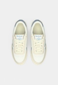 Par bijelih i bež Reebok Classic tenisica s plavim detaljima, prikazanih odozgo na jednostavnoj svijetloj pozadini.