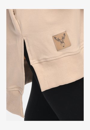 Beige Sweatshirt-Bund mit geripptem Bündchen und seitlichem Schlitz, versehen mit einem kleinen aufgenähten Patch mit einem schwarz umrandeten Hirschkopf.