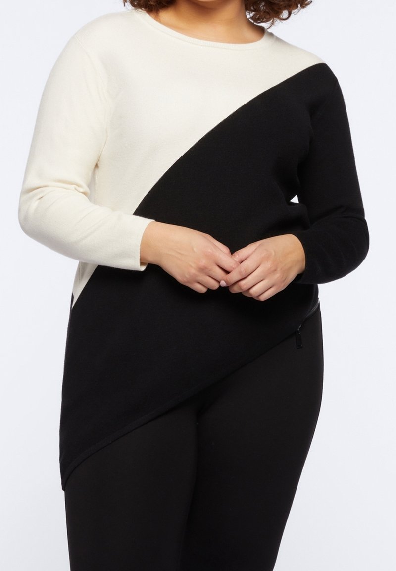 Pull noir et crème avec un design asymétrique, manches longues, texture douce et col rond. Détail de fermeture éclair sur le côté à l'ourlet.