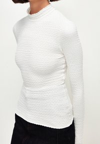 Top bianco a maniche lunghe con un motivo testurizzato e stropicciato, colletto a scallop e silhouette aderente, con un finish liscio all'orlo.