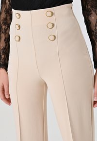 Beige hoge taille broek met een gladde textuur, met vijf gouden ring knopen en verticale naden voor een getailleerde pasvorm.