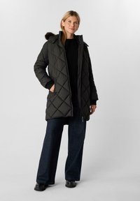 Parka nera trapuntata con zip frontale, cappuccio foderato in pelliccia e tasche laterali. Abbinata a jeans in denim scuro a gamba larga e calzature nere.