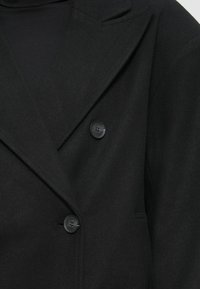 Manteau noir à double boutonnage avec une surface texturée, doté de revers crantés et de deux boutons ronds noirs à l'avant.