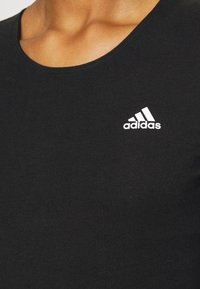 Débardeur noir côtelé avec un col rond. Présente un petit logo Adidas blanc sur le côté gauche de la poitrine. Texture lisse, coupe ajustée.