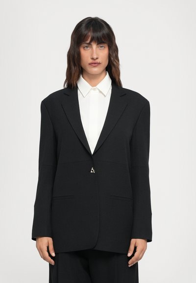 Zwarte op maat gemaakte blazer van gladde stof, met een enkele driehoekige zilveren knoop, gelapte revers en twee voorzakken.
