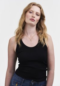 Must mustriba tank top ümmarguse kaelusega. Kombineeritud siniste teksadega, millel on kuldne ehted. Taust on lihtne valge.