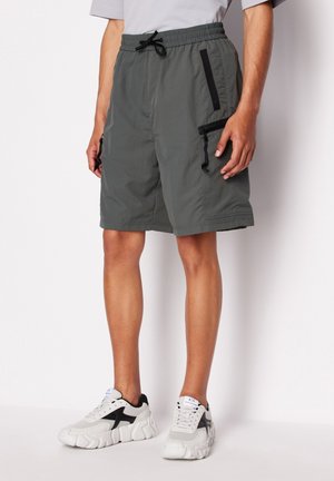 Pantaloni corti grigi leggeri con vita elastica, tasche con zip nere e vestibilità rilassata. Abbinati a scarpe da ginnastica grigie e nere.