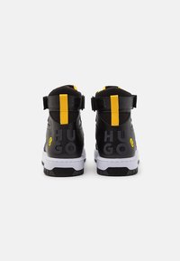 Svarta högskurna sneakers med gula accenter. Funktioner inkluderar ovandel i texturerat läder, dubbel remstängning och "HUGO"-logotyp på baksidan.