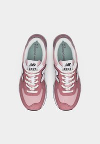 Paire de baskets New Balance 574 roses avec lacets blancs et logos, vue de dessus sur un fond blanc uni.