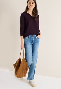 Langærmet, dyb lilla top med henley-udskæring; båret med lyseblå, brede jeans og cremede sneakers; holder en brun ruskinds taske.