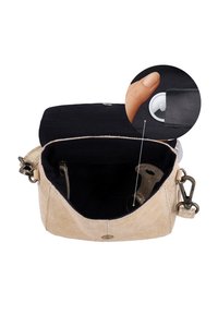 Petit sac à main beige avec intérieur noir montrant une main tenant un petit dispositif de suivi blanc à l'intérieur d'une poche.