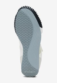 Semelle de sneaker blanche avec des grips en caoutchouc noir texturé, des motifs ondulés et un intercalaire gris. Le nom de la marque "Desigual" est embossé sur la semelle.