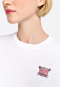 Balta trumpa rankovė t-shirt su apvalia iškirpte, ant kairės krūtinės pusės pavaizduota leopardinė grafika su rožiniais akinių nuo saulės.