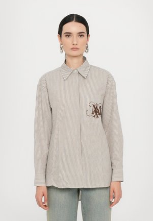 Camicia a righe, con bottone, di colore beige chiaro e marrone, dotata di una tasca sul petto con logo marrone. Maniche lunghe con polsini abbottonati.