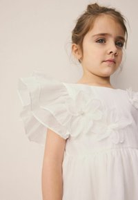 Weißes Kleid mit gerafften Ärmeln, strukturiertem Stoff und floralen Applikationen am Oberteil. Weiches, fließendes Design.