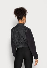 Czarna krótka kurtka z gładkiego, błyszczącego materiału z fakturowanymi rękawami. Posiada stojący kołnierz oraz elastyczny dół dla dopasowanego wyglądu.