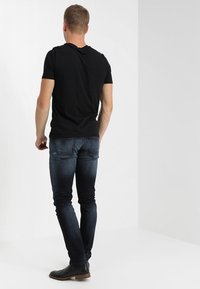 Svart kortärmad t-shirt, slim fit, tillsammans med mörkblå jeans. Jeansen har en lätt blekning och två bakfickor. Svarta ankelskor.