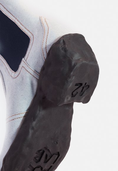 Zapato de escalada con parte superior de tela azul y blanca, costuras reforzadas y suela de goma negra texturizada con un talón numerado.