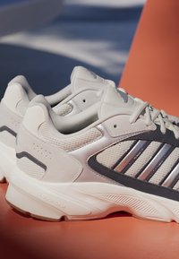Jasnoszare buty sportowe z siateczkowymi wstawkami, błyszczącymi ciemnoszarymi akcentami i brandingiem "CLOUDFOAM" na podeszwie, posiadające teksturowany bieżnik.