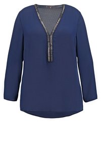 Blusa a maniche lunghe blu navy con scollatura a V profonda, caratterizzata da una finitura testurizzata argentata lungo il collo e un orlo arrotondato.