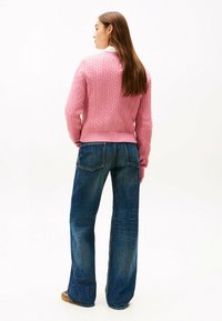 Maglione rosa a maglia con orlo a coste abbinato a jeans in denim blu a gamba larga. Visibili dettagli di texture liscia e vestibilità rilassata.