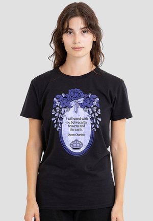Young woman wearing a black t-shirt with a purple floral frame, a crown illustration, and text reading a Queen Charlotte quote.