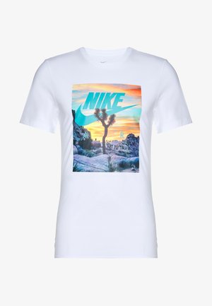 T-shirt en coton blanc avec un graphique rectangulaire représentant une scène désertique et le logo "NIKE" dans des teintes de bleu-vert et d'orange.