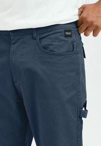 Navy blue cargo pants made of lightweight fabric, featuring side pockets, a front pocket, and a small logo patch on the waistband.