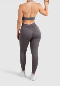 Conjunto de sujetador deportivo y leggings en gris, con un diseño ajustado que incluye una cinturilla alta y un acento de logo. Tela suave y elástica con costuras mínimas.