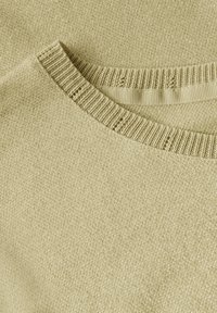 Ljust beige, texturerad, stickad tröja med krage som har ribbdetaljer och en slät yta. Materialet verkar mjukt, med en subtil lyster genom hela.