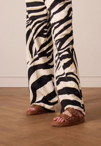 Zwart-wit gestreepte wijde broek met een zebra-patroon, gecombineerd met bruine geweven slidesandalen met een gesp en gevlochten zooldetails.