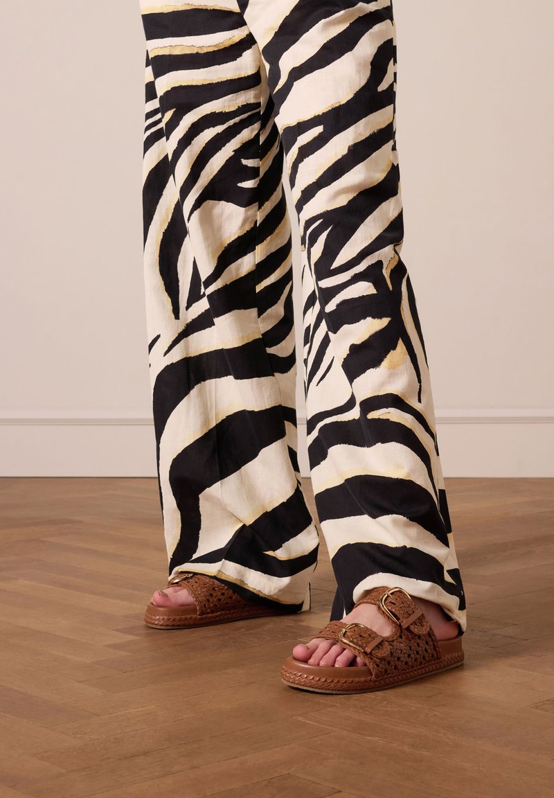 Zwart-wit gestreepte wijde broek met een zebra-patroon, gecombineerd met bruine geweven slidesandalen met een gesp en gevlochten zooldetails.