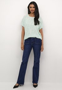 Top corto verde menta con un motivo sottile, abbinato a jeans a zampa d'elefante blu scuro. Tacchi neri a punta completano l'outfit.