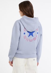 Felpa blu chiaro con un design grafico che presenta una stella blu e testo rosa, realizzata in materiale morbido, con tasca a marsupio e cappuccio.