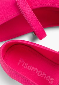 Bailarinas de tela rosa con correa, que cuentan con una superficie texturizada y un interior suave, etiquetadas como "Psamanos". El diseño simple enfatiza el color.