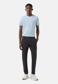 Hellblaues T-Shirt mit kurzen Ärmeln und kleinem Logo auf der Brust, kombiniert mit dunkler Hose und weißen Sneakern. Klare Gestaltung, bequeme Passform.