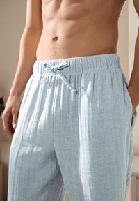 Light blue lounge pants made of textured fabric; features an elastic waistband with a drawstring and side pockets.