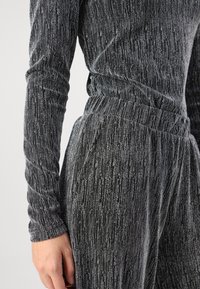 Ensemble bi-matière noir et argent composé d'un haut à manches longues et d'un pantalon avec un motif de rayures verticales texturé et une taille élastique.
