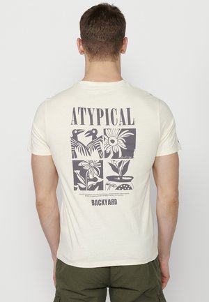 Kremna majica s grafičnim dizajnom na zadnjem delu, s crnimi ilustracijami cvetja in ptic ter napisom "ATYPICAL BACKYARD."
