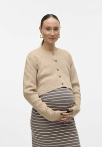 Bež prugast kratki kardigan z gumbi, oblečen preko sive in bele prugaste obleke, poudarja zaobljeno trebušček in sproščen kroj.