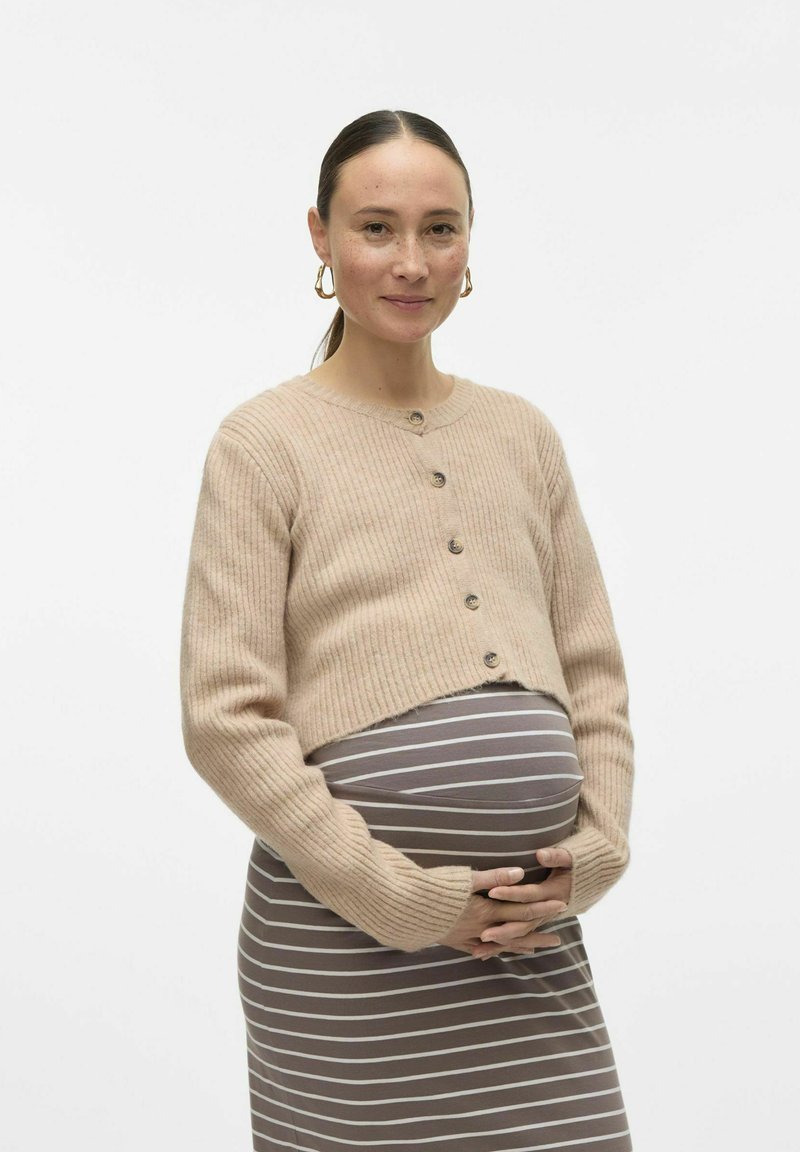 Bež prugast kratki kardigan z gumbi, oblečen preko sive in bele prugaste obleke, poudarja zaobljeno trebušček in sproščen kroj.