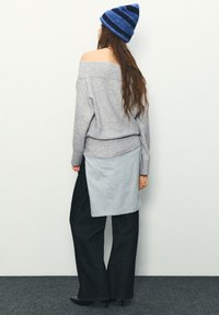 Schulterfreier, hellgrauer Pullover mit weicher Textur, kombiniert mit dunkler, weiter Hose und blau gestreiftem Hut, zeigt geschichtetes Design.