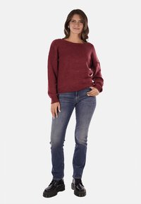 Maglione a maglia color mogano con un ampio scollo e maniche lunghe, abbinato a jeans blu medio e stivaletti neri chunky. Design semplice e strutturato.