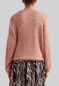 Roze gebreide trui met een losvallende pasvorm en lange mouwen, gecombineerd met een geplooide rok met een zwart-roze zebra patroon.