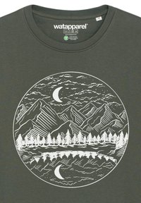 Donkergroene t-shirt met een witte cirkelvormige grafische afbeelding van bergen, bomen, een meer en een maansikkel tegen een bewolkte lucht.
