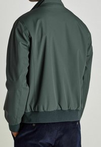Giacca bomber verde scuro con una finitura liscia e opaca, orlo a bande e polsini a costine. Presenta un colletto classico e un design snello.